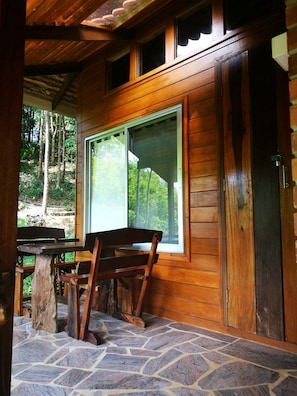 A wooden cabin with a stone-tiled porch, a wooden bench, and a table.