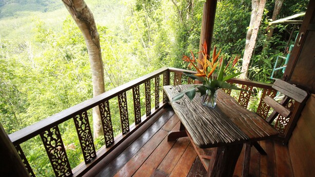 Une terrasse en bois avec un banc et une table, entourée d’une balustrade décorative.