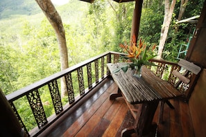 Una terraza de madera con un banco y una mesa, rodeada por una barandilla decorativa.