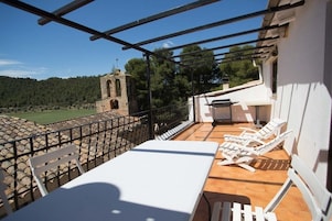 Una terraza con mesa y sillas, una parrilla y vistas a una torre y un bosque.