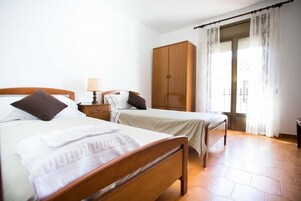Habitación de hotel con dos camas, un armario, una mesita de noche y una ventana con cortinas.