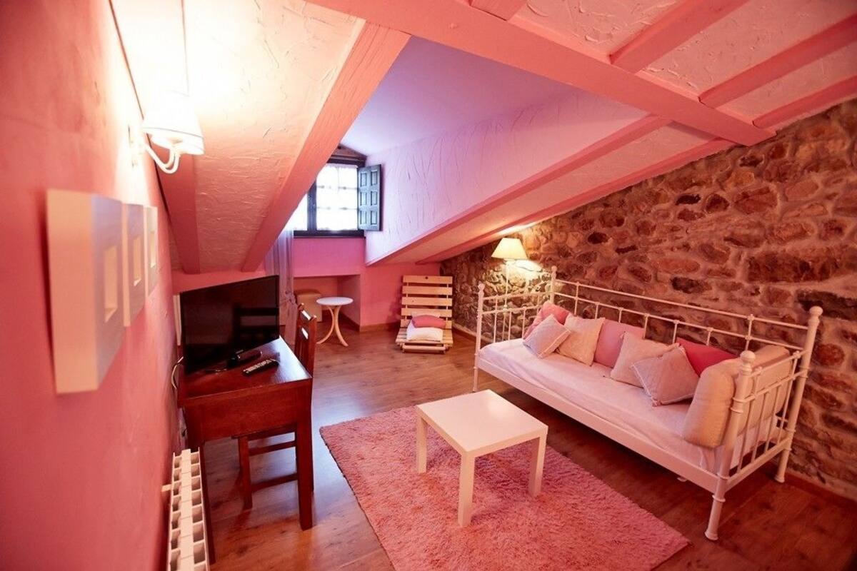 A cozy attic bedroom with a stone wall, a white bed, a wooden desk, and a small table.