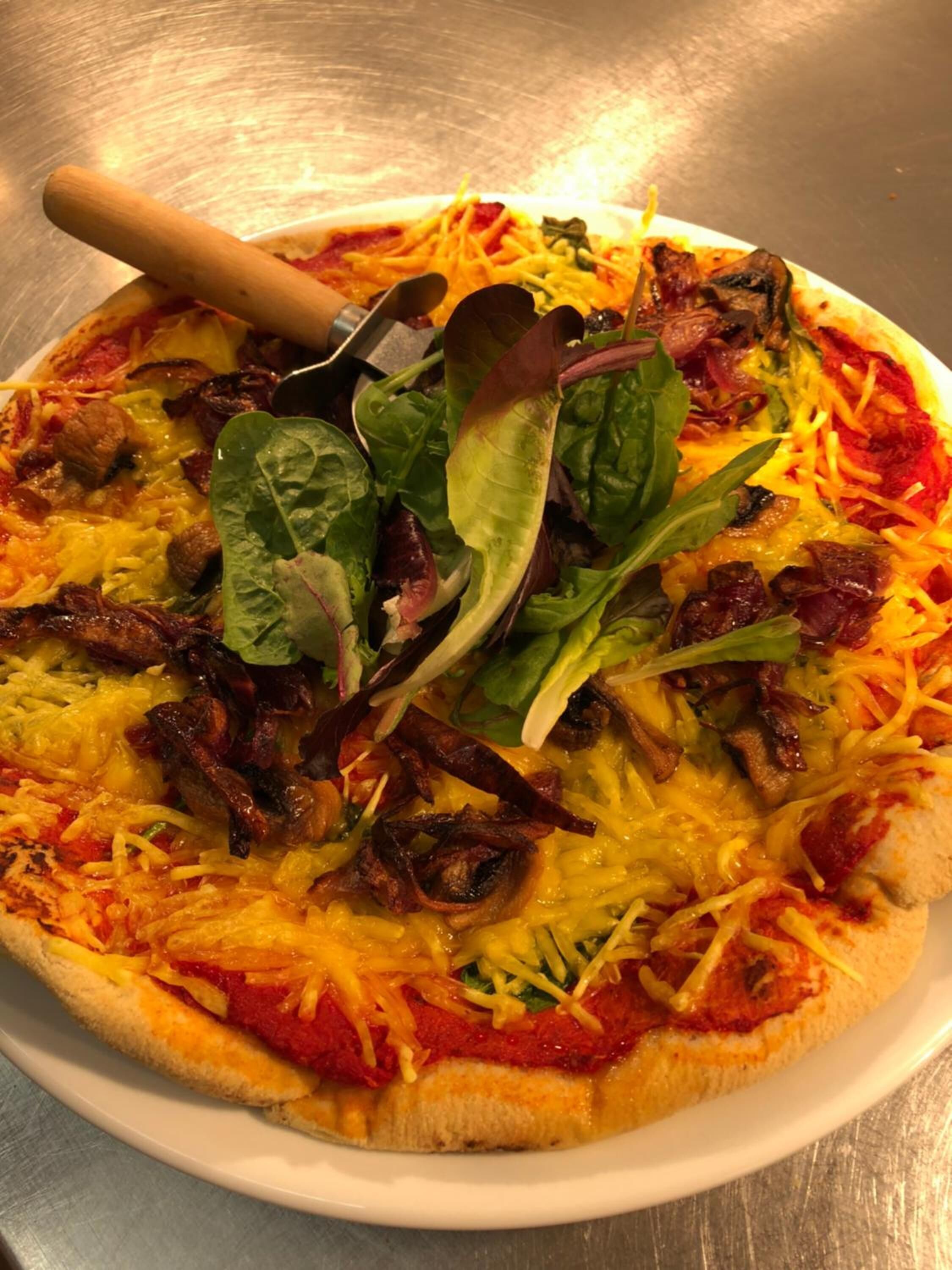 Eine Pizza mit verschiedenen Belägen, darunter Käse, Speck, Pilze und grünes Gemüse, auf einem weißen Teller.