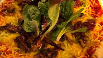 Una pizza con varios ingredientes, incluyendo queso, tocino, champiñones y vegetales verdes, sobre un plato blanco.