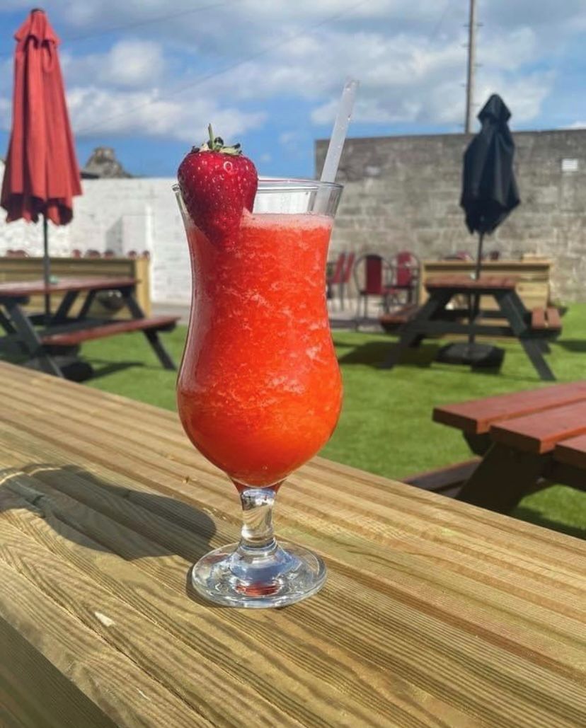 A tall glass with a strawberry garnish on a wooden table outdoors.
