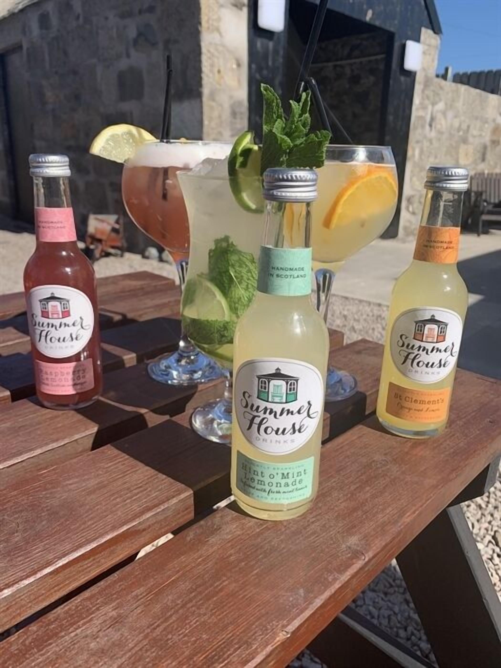 Tres botellas de Summer House sobre una mesa de madera al aire libre.