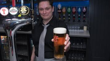 A bartender holding a beer mug with a logo, behind a tap with multiple beer brands.