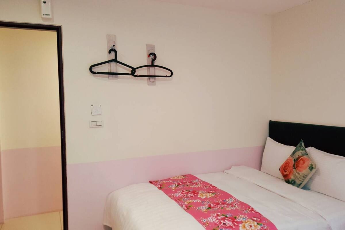 Une chambre à coucher avec un lit, un mur à rayures roses et blanches, et deux cintres noirs sur un porte-manteau fixé au mur.