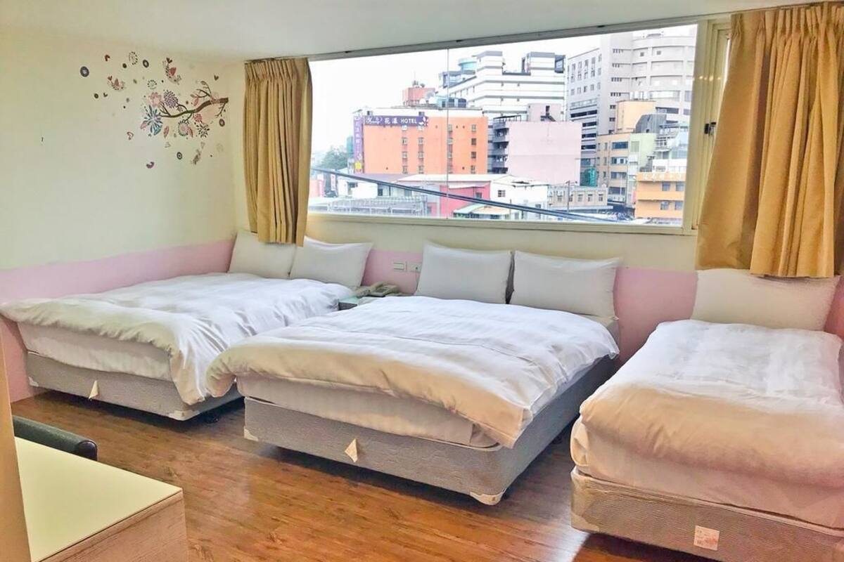 Une chambre d’hôtel avec deux lits, une petite table en bois et une vue sur les immeubles par la fenêtre.