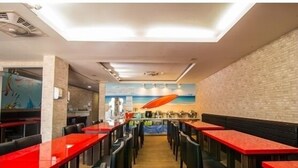 A restaurant with red tables and black chairs, a brick wall, and a mural of a surfboard. - Happy Holiday Hotel (Taoyuan City)
