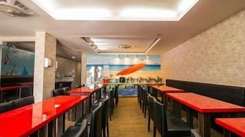 A restaurant with red tables and black chairs, a brick wall, and a mural of a surfboard.