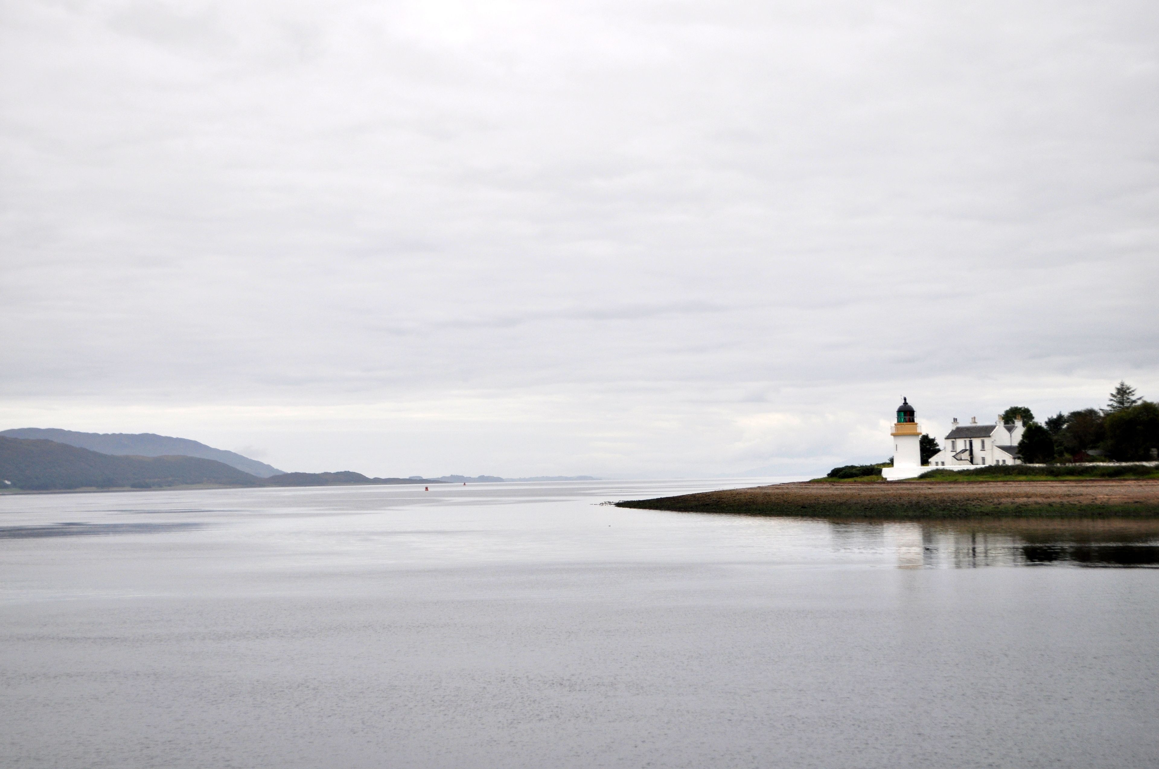 A coastal scene with a lighthouse and a white building on a sandy shore.