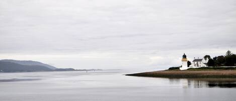 A coastal scene with a lighthouse and a white building on a sandy shore.