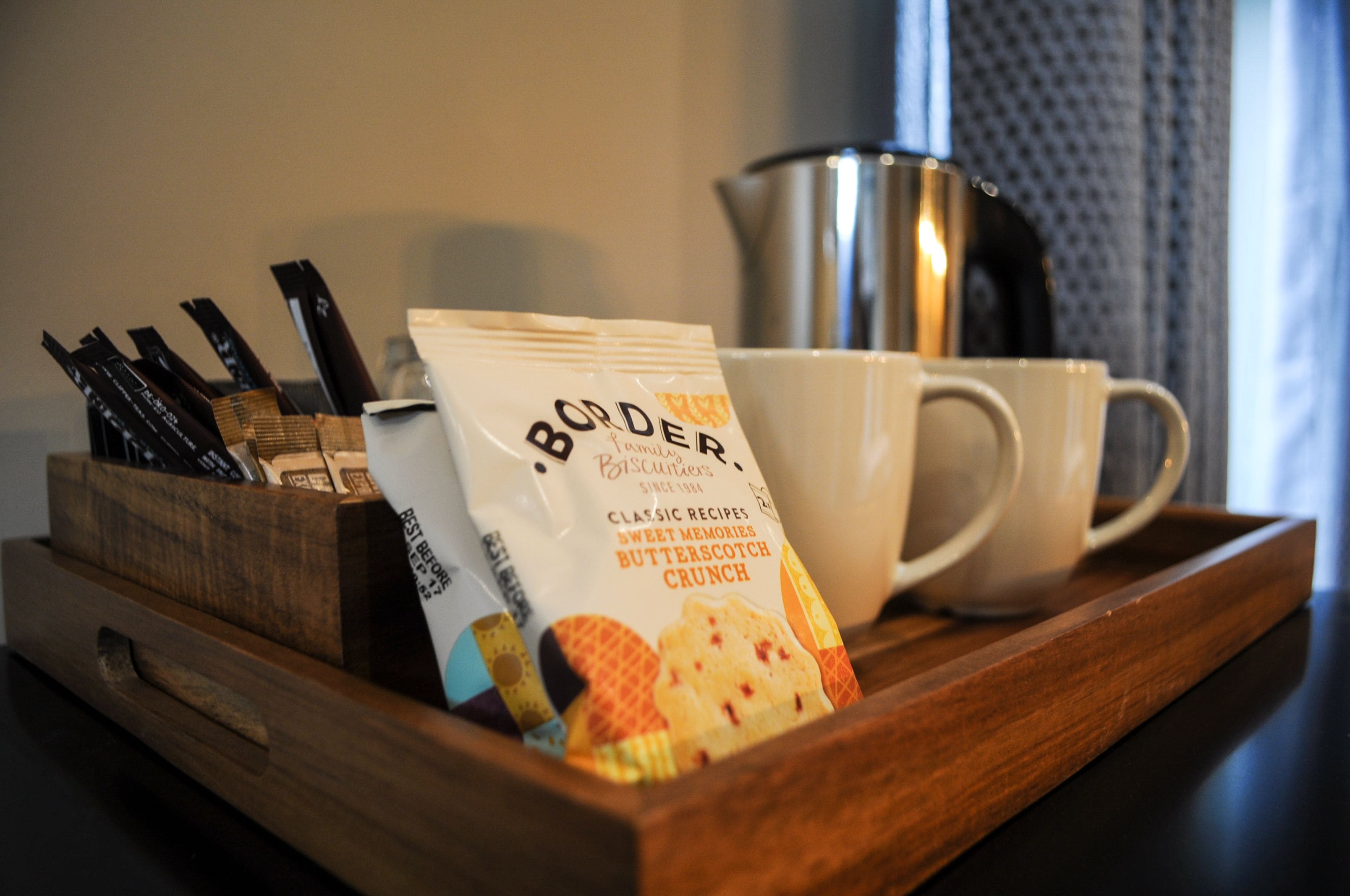 A tray with a packet of Border Biscuits, a white cup, and a stainless steel container.