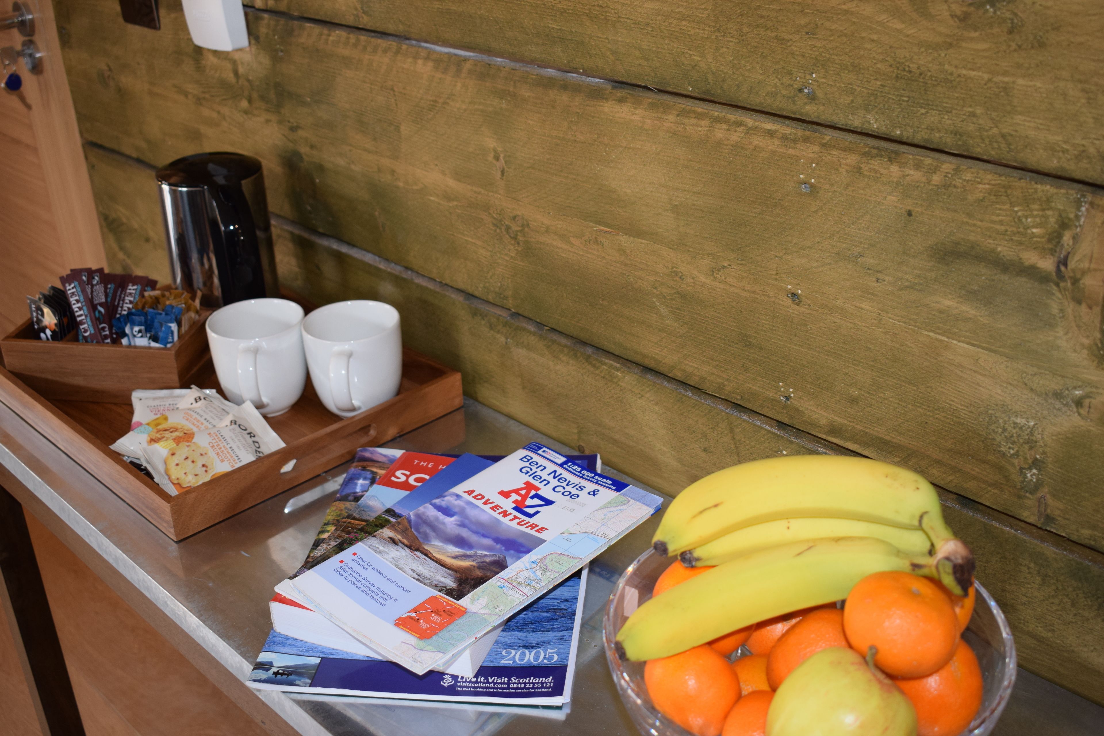 A breakfast tray with a coffee maker, two cups, a bowl of fruit, and travel brochures.