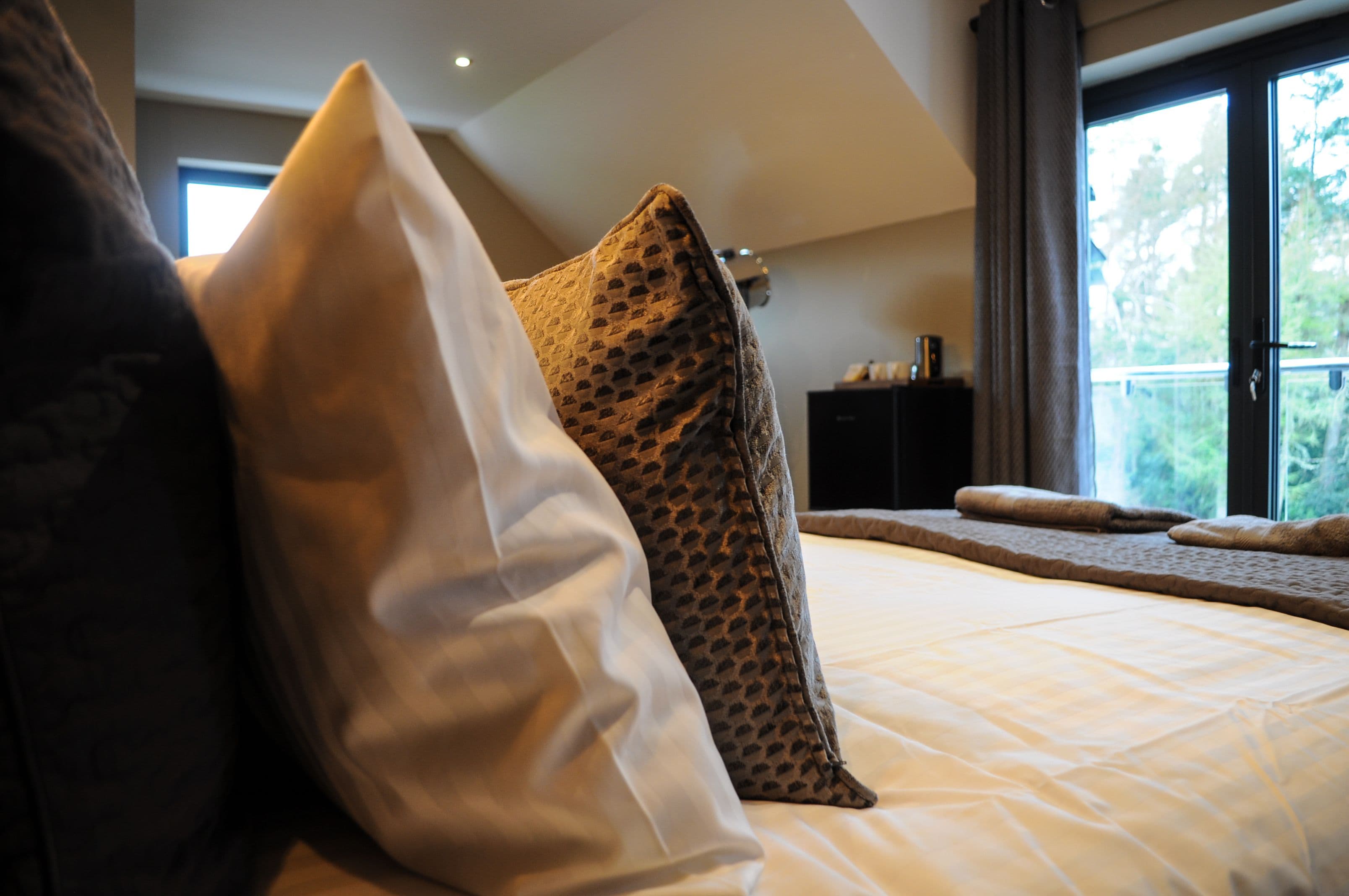 A bedroom with a bed, pillows, a window, and a view of greenery outside.
