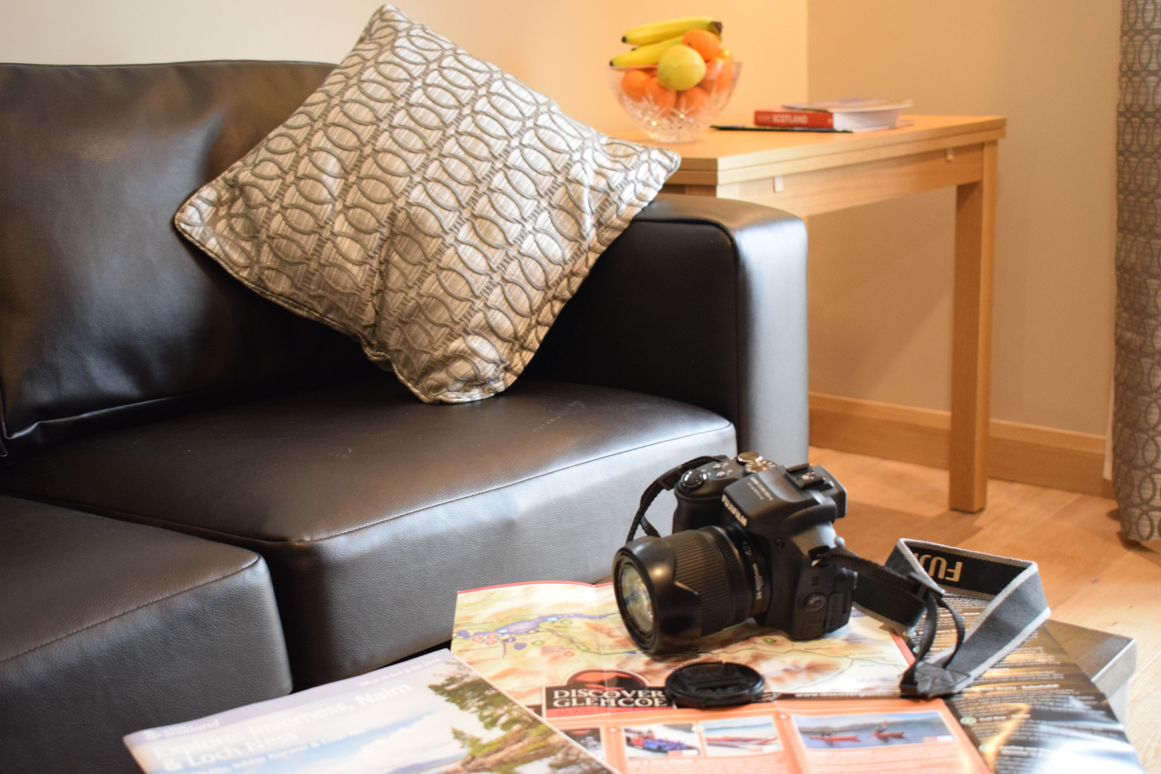 A black leather sofa with a patterned pillow, a camera, and travel brochures on a coffee table.