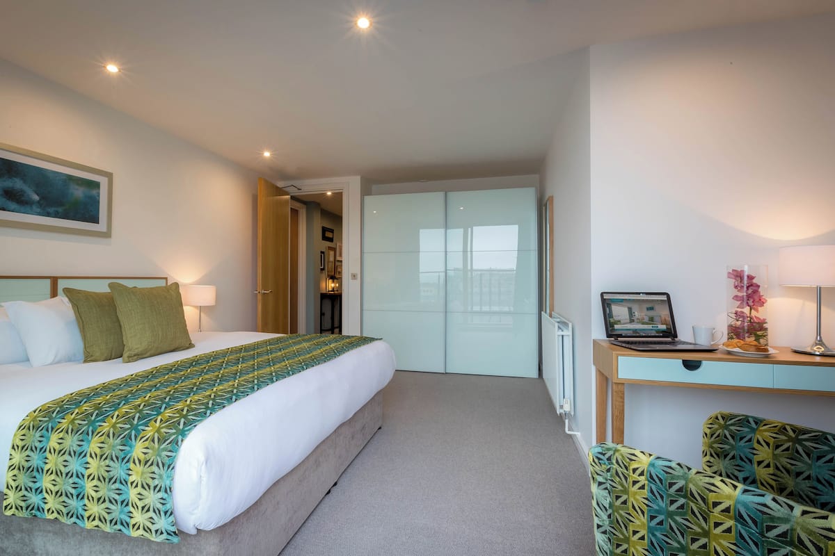 Habitación de hotel con cama, escritorio, silla, una laptop y un cuadro en la pared.