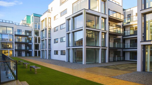 A modern multi-story residential building with large windows, a central courtyard with a wooden deck, and a grassy area. - Talbot Suites at Stonebridge (Wexford)