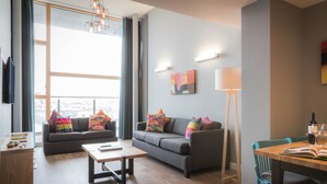 A modern living room with a sofa, coffee table, and dining area. - Talbot Suites at Stonebridge (Wexford)