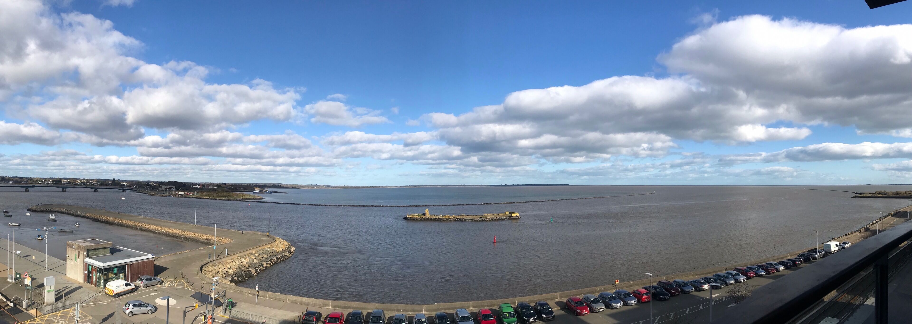 A coastal view with a parking area, a small building, and a calm body of water.