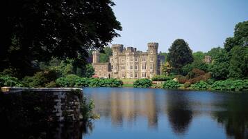 A large, historic building with a moat, surrounded by lush greenery and trees.