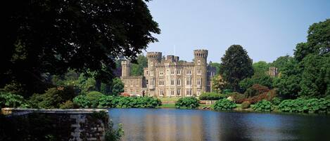 A large, historic building with a moat, surrounded by lush greenery and trees.