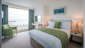 A hotel room with a bed, a desk, a chair, a window with a view, and a painting on the wall. - Talbot Suites at Stonebridge (Wexford)
