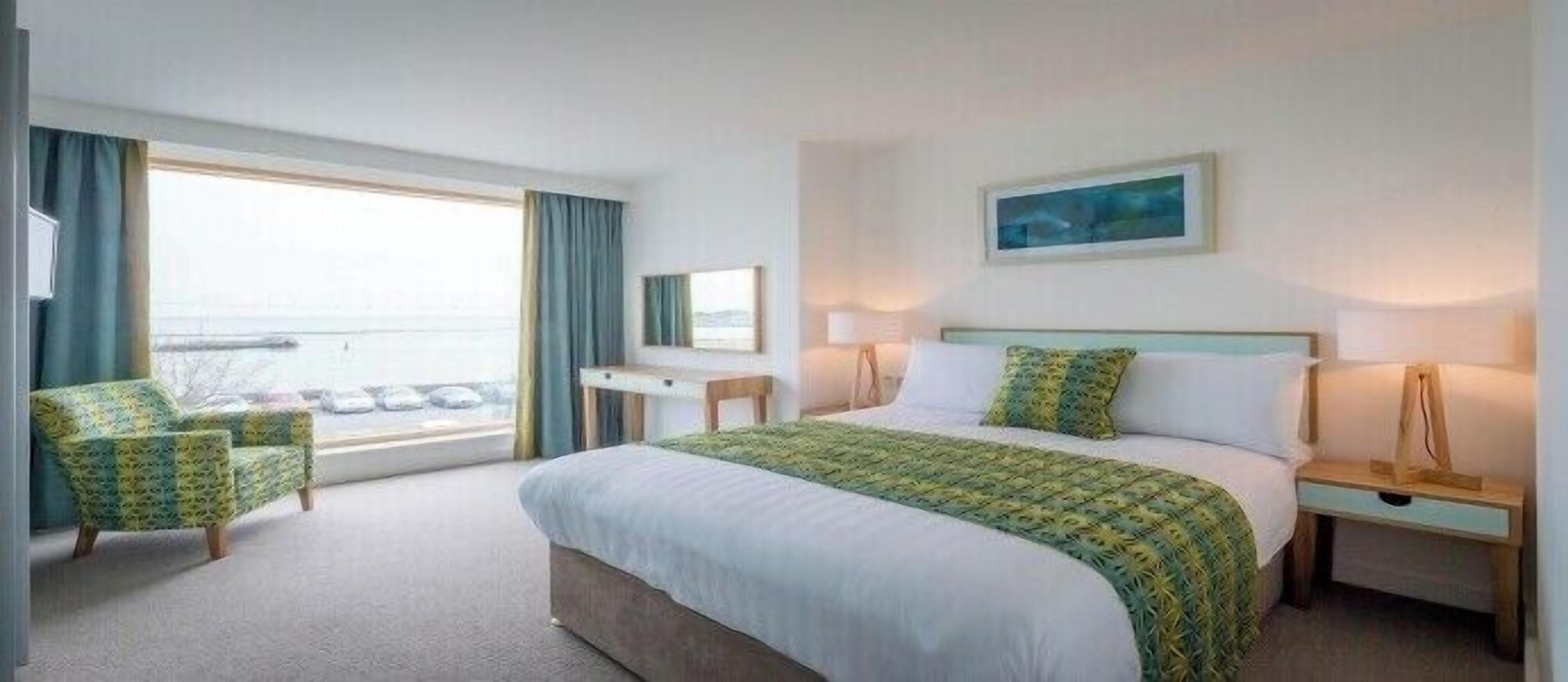 A hotel room with a large bed, a desk, a chair, a window with curtains, and a painting on the wall.
