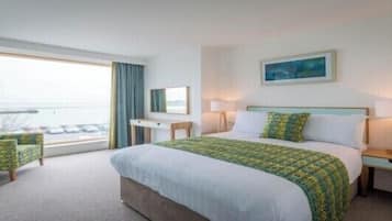A hotel room with a large bed, a desk, a chair, a window with curtains, and a painting on the wall.