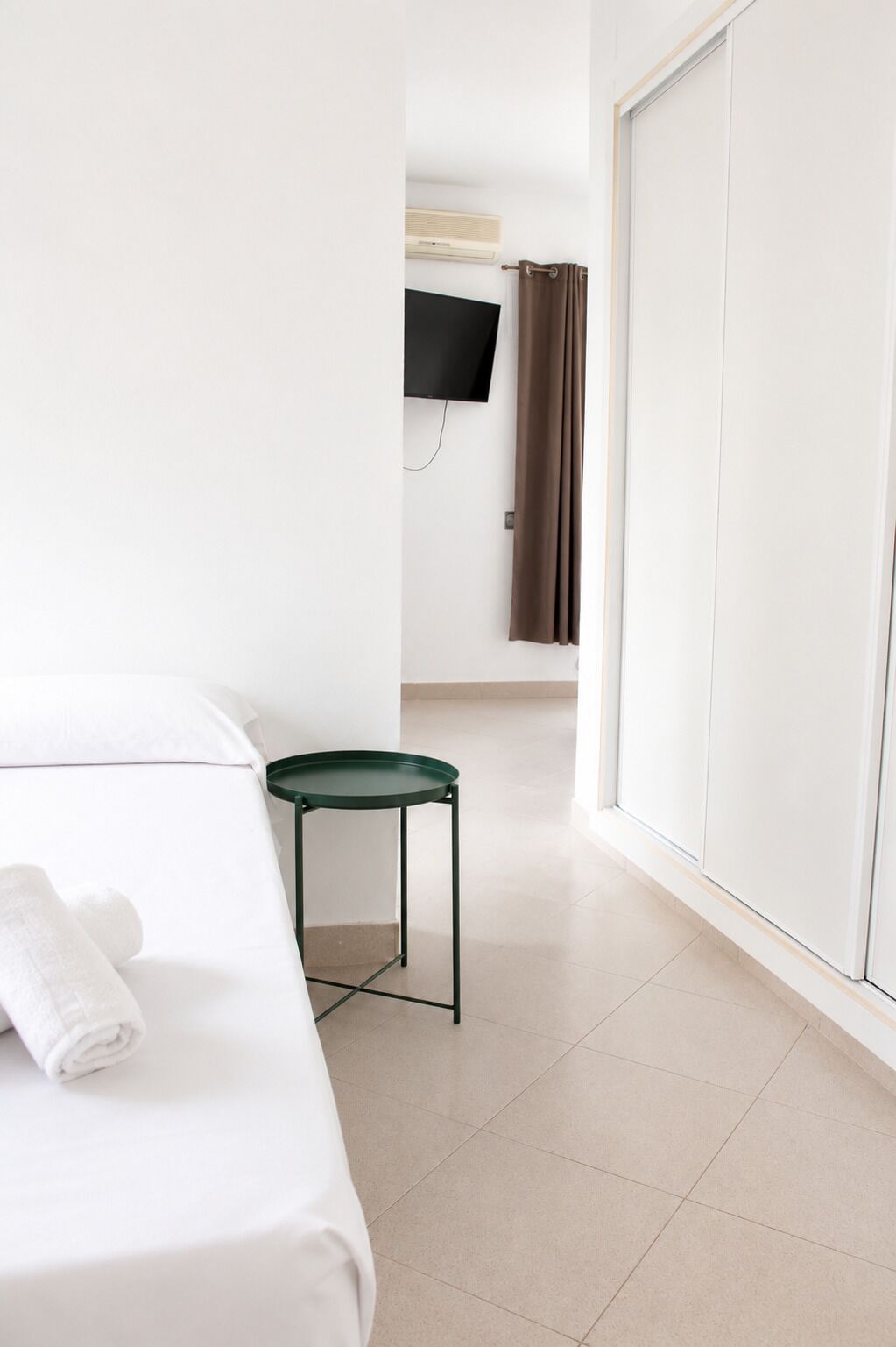 A hotel room with a bed, a small table, a TV mounted on the wall, and a sliding door.