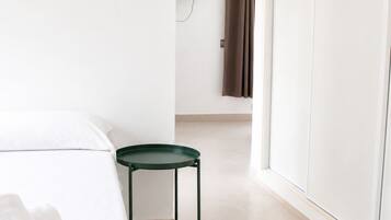 A hotel room with a bed, a small table, a TV mounted on the wall, and a sliding door.