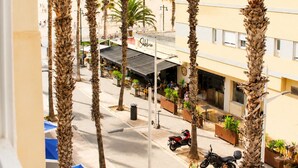 A street view with palm trees, a building with a sign 'Subito', and a clear sky. - Malvarrosa Beach Rooms (Valencia)