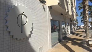 A building facade with a large metallic gear-shaped sign, a tiled wall, and a clear sky. - Malvarrosa Beach Rooms (Valencia)