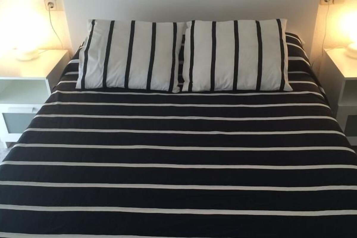 A bed with black and white striped bedding, two bedside tables, and two wall-mounted lamps.