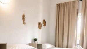 A hotel room with two beds, a bedside table with a lamp, a wall-mounted decoration, and a window with curtains. - Malvarrosa Beach Rooms (Valencia)