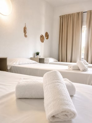 A hotel room with two beds, a bedside table with a lamp, a wall-mounted decoration, and a window with curtains. - Malvarrosa Beach Rooms (Valencia)