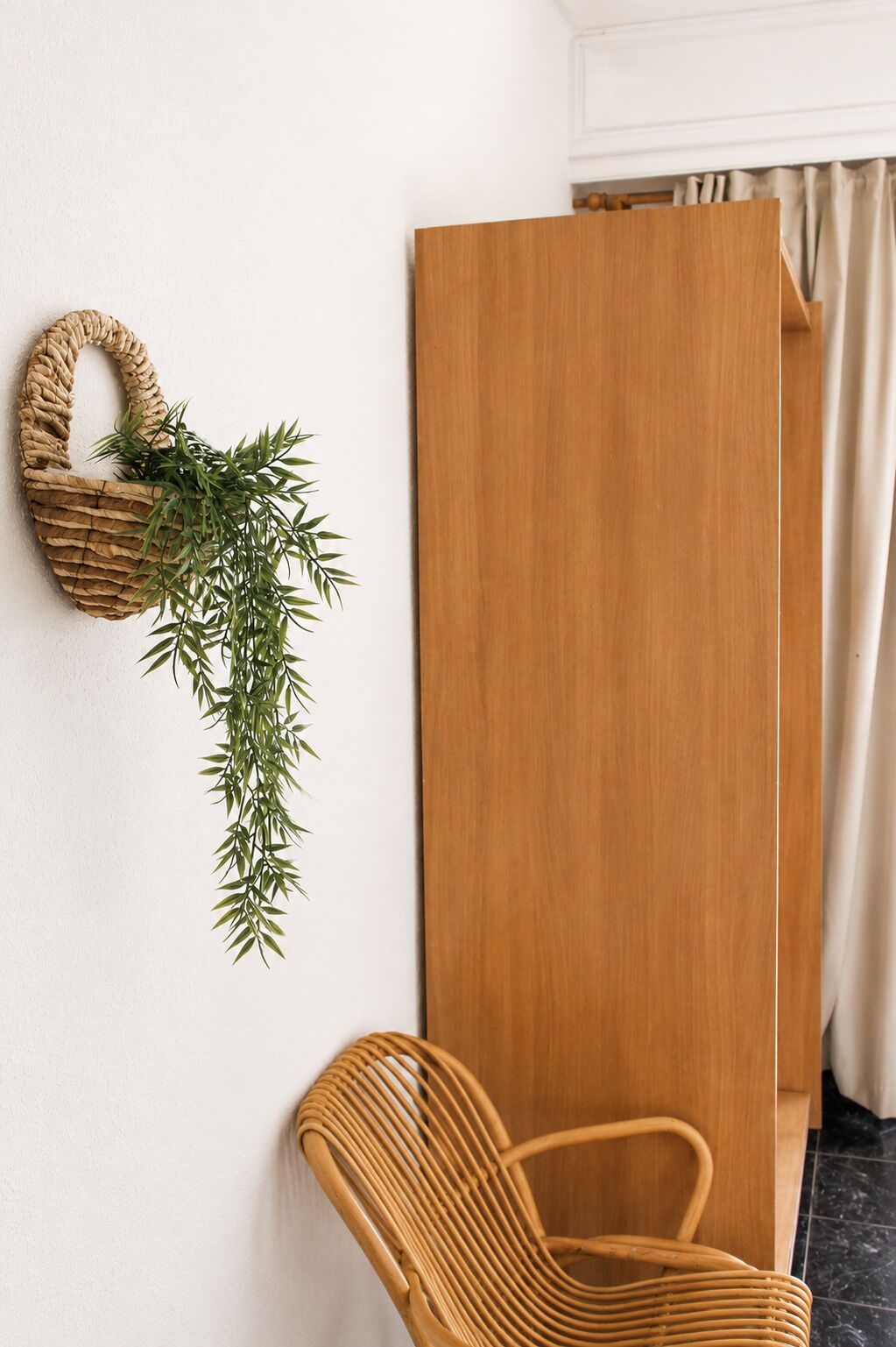Una habitación con un armario de madera, una silla de mimbre y una planta en la pared.