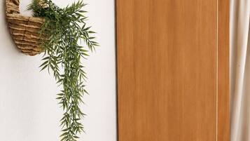 Una habitación con un armario de madera, una silla de mimbre y una planta en la pared.