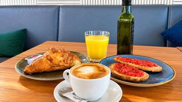 A table with a croissant, a cup of coffee, a glass of orange juice, and two slices of toast with tomato spread.