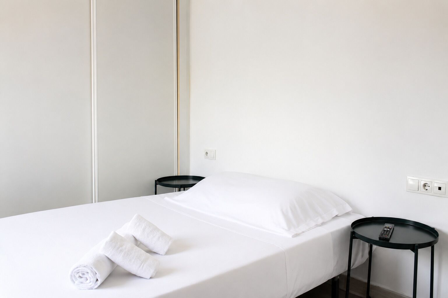 A single bed with white bedding, two black side tables, and a remote control on one of the tables.