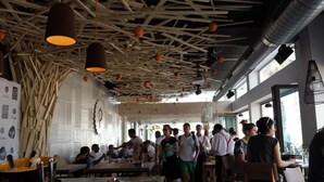 A restaurant with a high ceiling, wooden beams, and hanging orange lights. Tables are arranged for dining. - Malvarrosa Beach Rooms (Valencia)