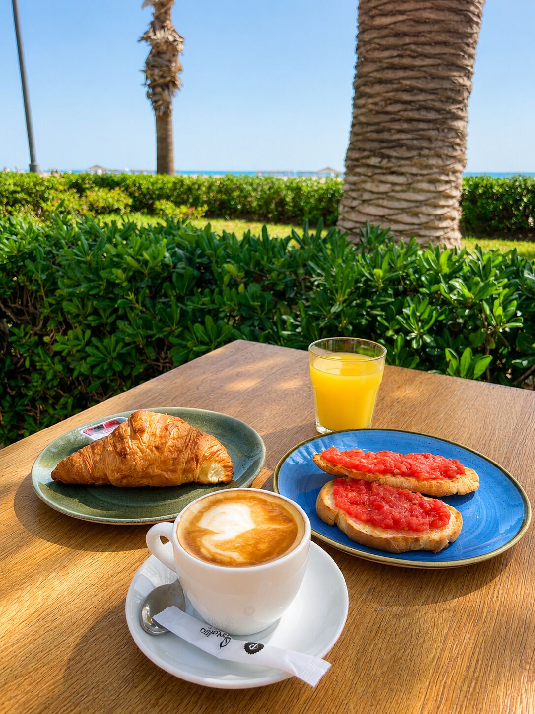 A table with croissants, toast with tomato, a cup of coffee, and a glass of orange juice.
