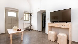 A room with a wooden desk, two matching stools, a television, a coat rack, and a door. - Villa Aegeon Grande (Santorini)