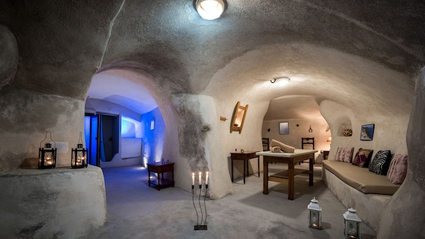 An interior with a stone archway, a wooden table, a sofa, and candles on the floor. - Villa Aegeon Grande (Santorini)