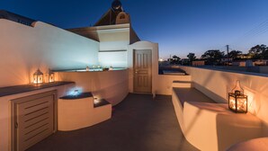 A rooftop terrace with a curved wall, a door, and lanterns providing ambient lighting. - Villa Aegeon Grande (Santorini)