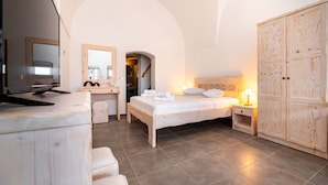 A bedroom with a bed, bedside table, wardrobe, and a television on a dresser. - Villa Aegeon Grande (Santorini)