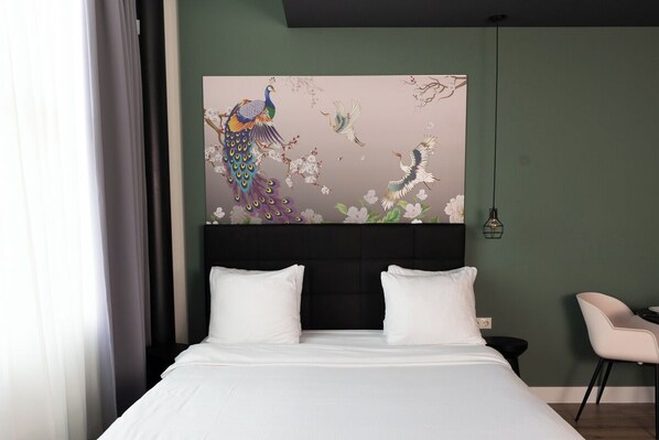 Une chambre d’hôtel avec un grand lit, deux oreillers blancs, une tête de lit noire et une œuvre d’art représentant des oiseaux et des fleurs, accrochée au mur.