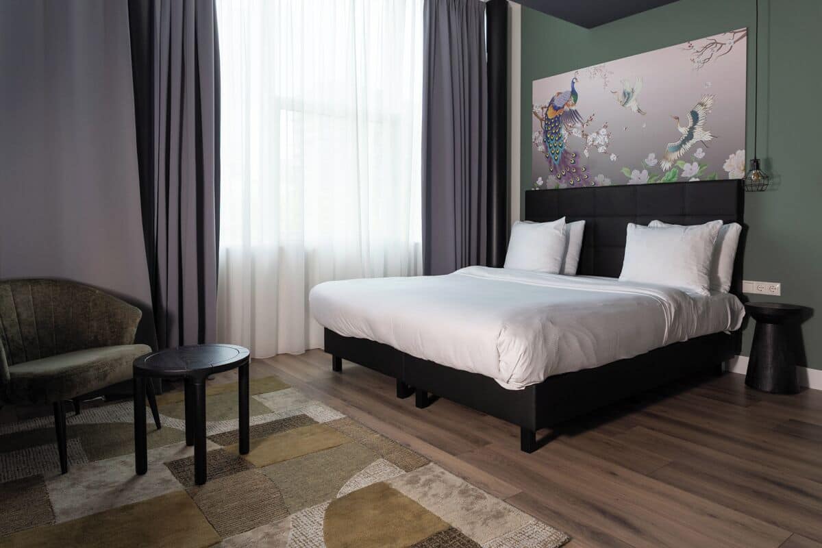 A modern bedroom with a large bed, a sofa, a small table, and a decorative painting on the wall.
