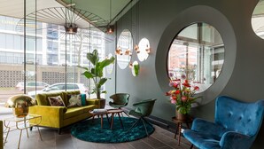 A modern interior with a yellow sofa, green armchairs, a blue chair, and a round table. - Hotel2Stay (Amsterdam)